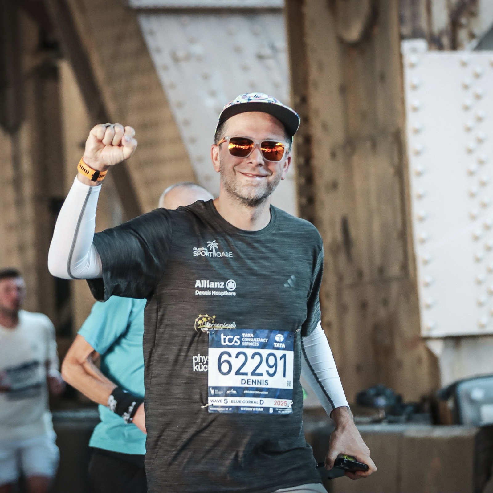 Dennis jubelt mit erhobener Faust auf einer Brücke beim New York Marathon.